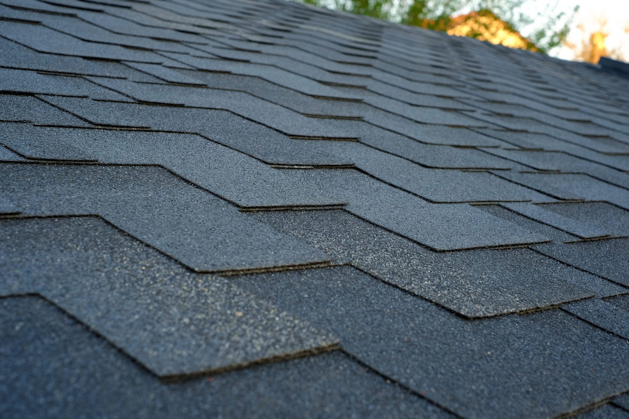 Close-up view of dark asphalt roof shingles on a residential home, showing the texture and overlapping pattern of the roofing material under natural daylight.